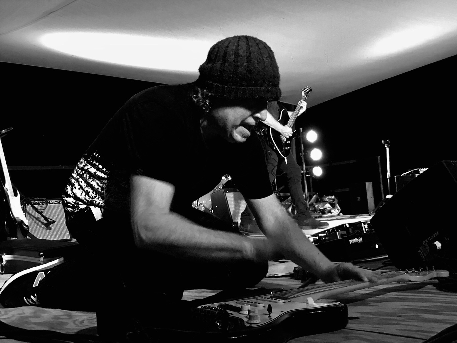 Garrett Tucker crouched over his guitar on stage, a second guitarist and stage lights behind him.