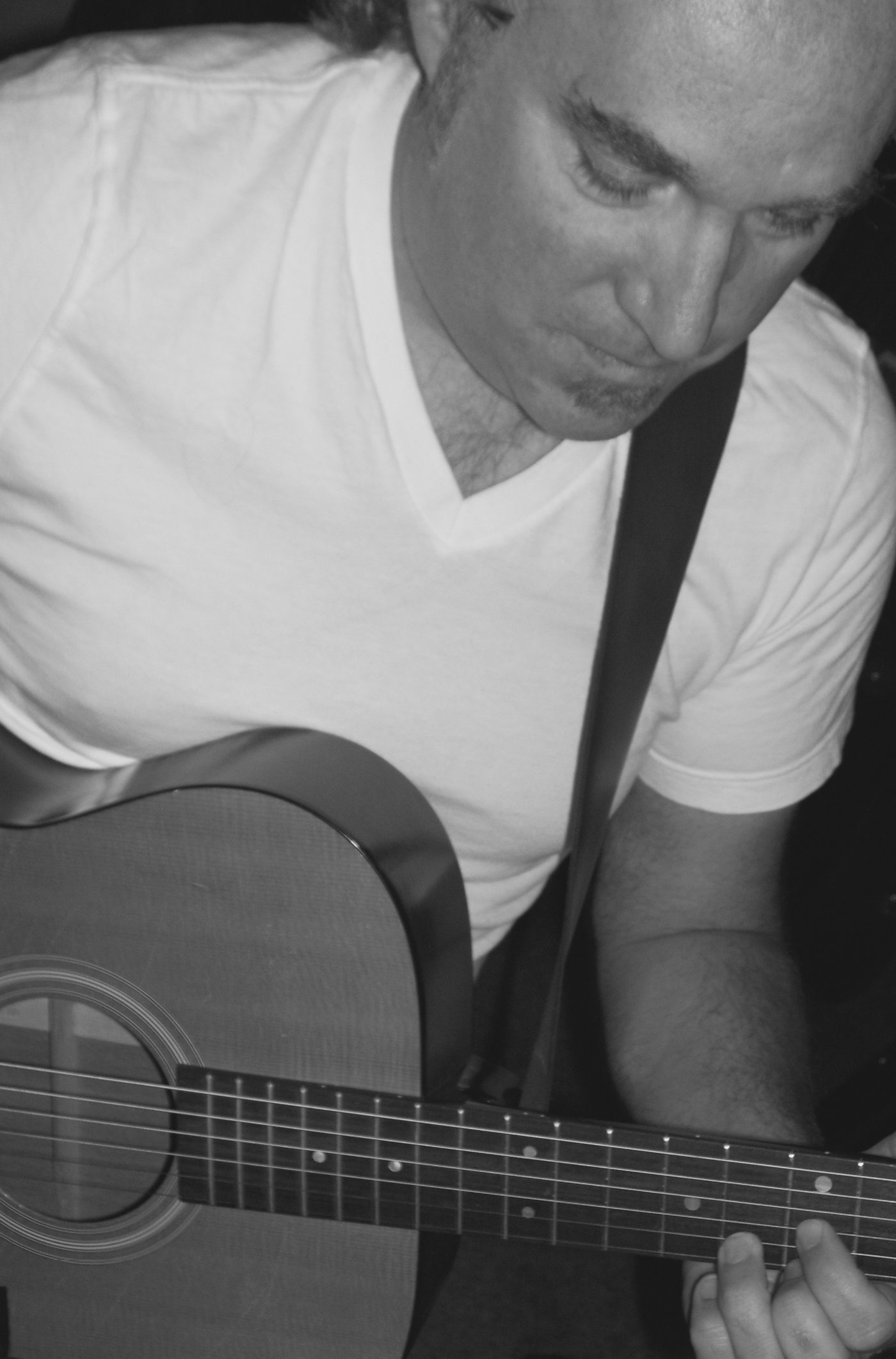 Garrett Tucker playing an acoustic guitar, photographed in black and white.